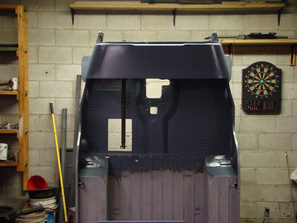 Back of a vehicle tub with diamond plate flooring, in a garage with a dartboard on the wall