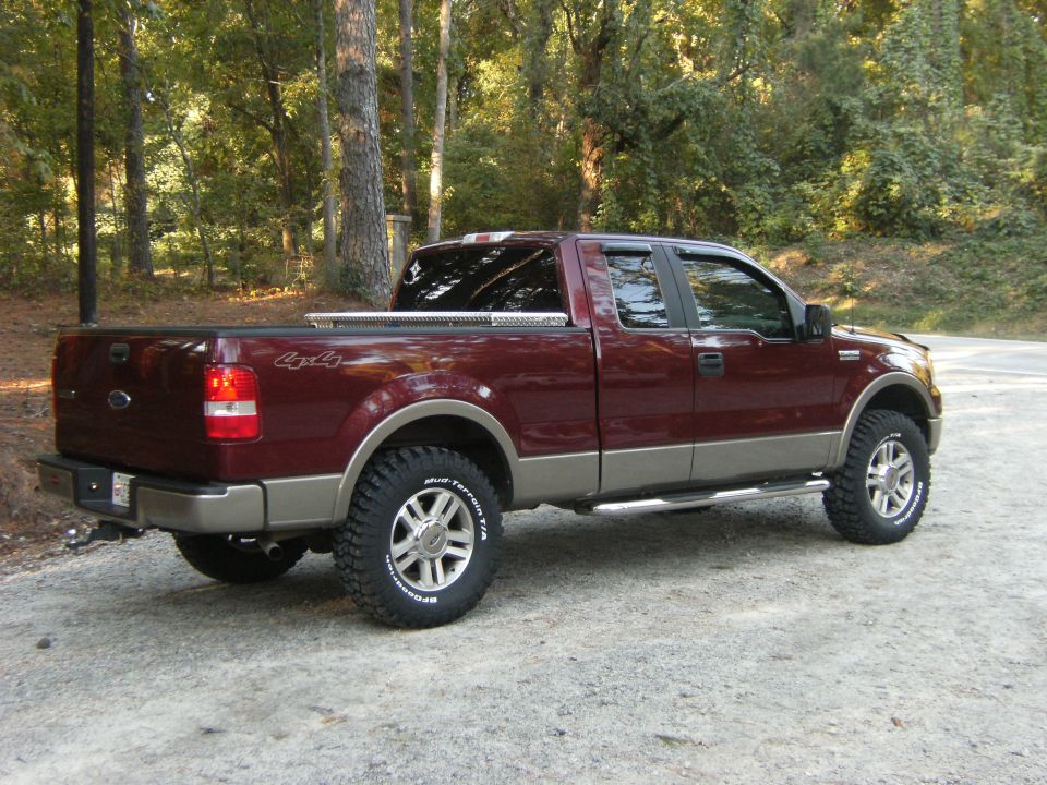 Maroon Ford F-150 4x4 pickup, rear 3/4 view on gravel road with mud-terrain tires