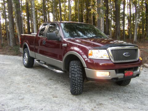 2005 Ford F-150 - Maroon 2005 Ford F-150 pickup truck with tan trim and large tires sits on a gravel surface.