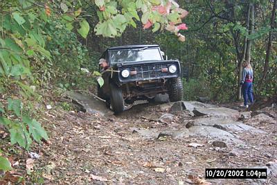 1972 Ford Bronco - A black Ford Bronco tackles a challenging off-road course in a wooded area.