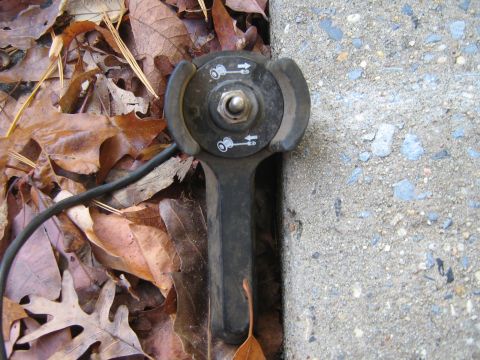 1990 Ford Bronco - Close-up of a lawnmower throttle control lever lying on fallen leaves.