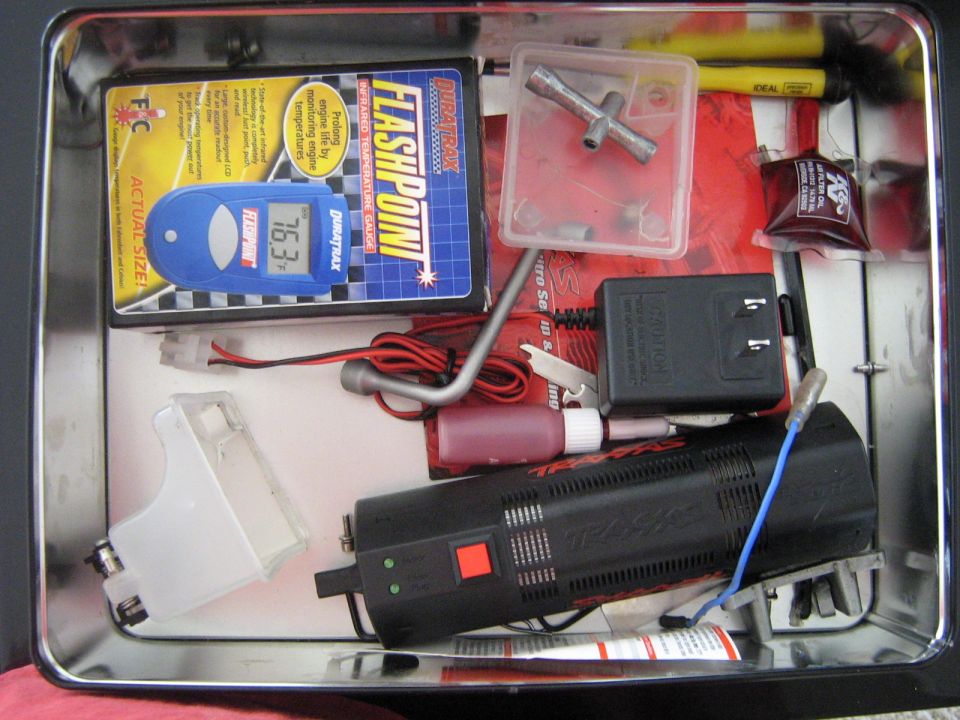 RC car charger, temperature gauge, and tools inside a metal tin