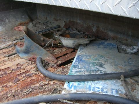 1988 Ford Bronco - Rotted wooden bed floor of an old truck viewed from inside the box, split and rusted through with daylight showing beneath the boards. Rust…