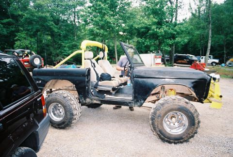 1972 Ford Bronco - A modified black Ford Bronco sits outdoors with a person inside, showing its lifted suspension and off-road tires.