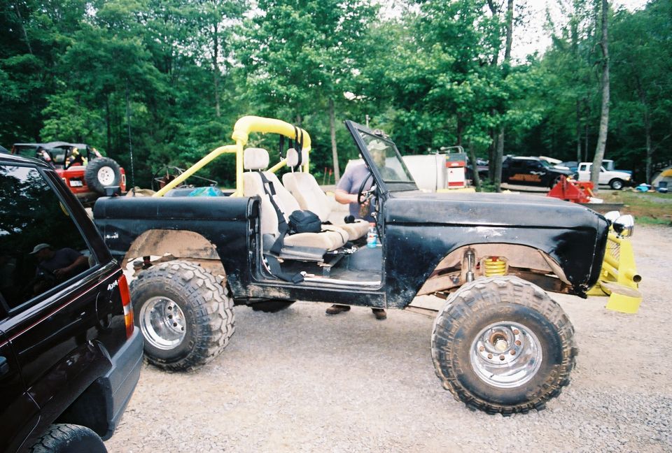Black Ford Bronco with lifted suspension and large tires, open doors, yellow roll cage