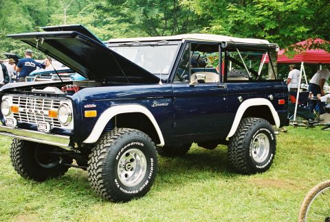 1972 Ford Bronco - A dark blue 1972 Ford Bronco is parked on grass with its hood open, revealing the engine bay.
