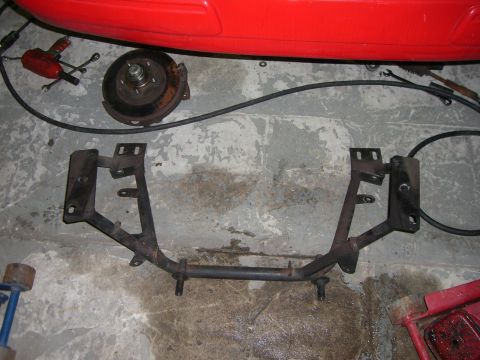 1988 Ford Bronco - A metal automotive part, possibly from a suspension system, lies on a concrete floor next to a brake rotor.