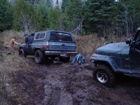 1988 Chevrolet Blazer - Two off-road vehicles are stuck in a muddy trail, with one vehicle attempting to pull the other.