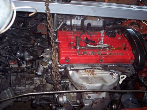 1995 Mitsubishi Eclipse - The engine is suspended by a chain hoist, with tools resting on the red valve cover.