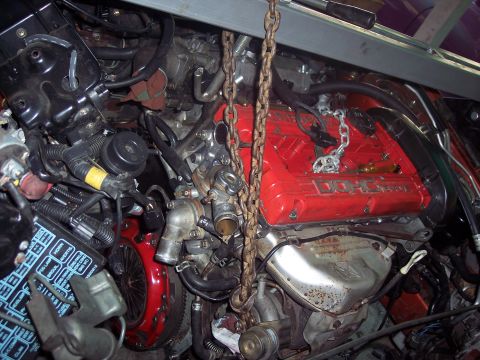 1995 Mitsubishi Eclipse - Engine with DOHC 16V marking, suspended by chains. Fuse box visible on left.