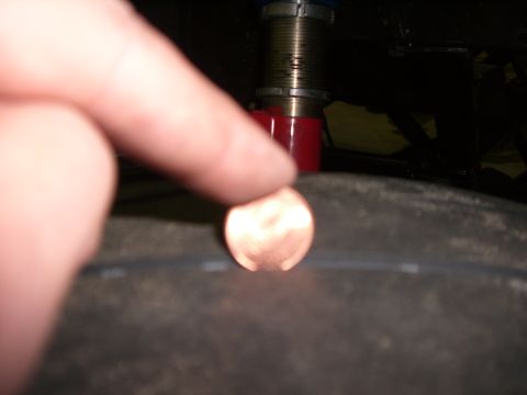 1988 Ford Bronco - A penny is placed on a tire tread, next to a red shock absorber, suggesting a part measurement.