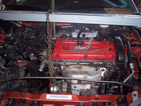 1995 Mitsubishi Eclipse - The engine is being supported by a hoist in the engine bay, with the red DOHC engine cover prominently displayed.