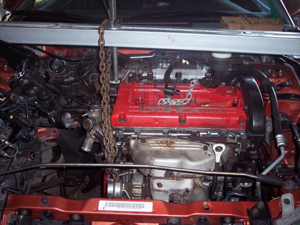 Engine bay with engine hoist rigged up, red DOHC engine cover visible