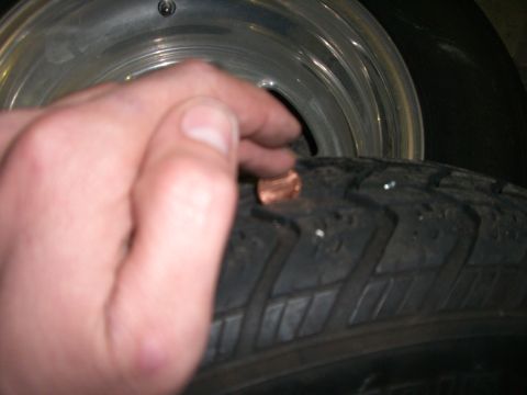 1988 Ford Bronco - A penny is placed on a tire's tread, possibly to check tread depth, next to a shiny wheel rim.