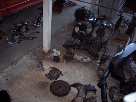1995 Mitsubishi Eclipse - Various automotive components are scattered across a garage floor, suggesting a vehicle in disrepair or undergoing maintenance.