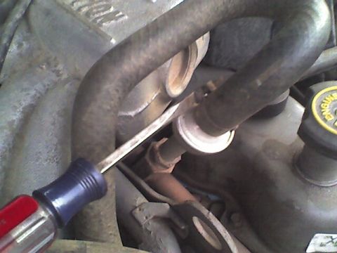 1989 Ford Bronco - Close-up of engine components with a screwdriver being used on a fitting.