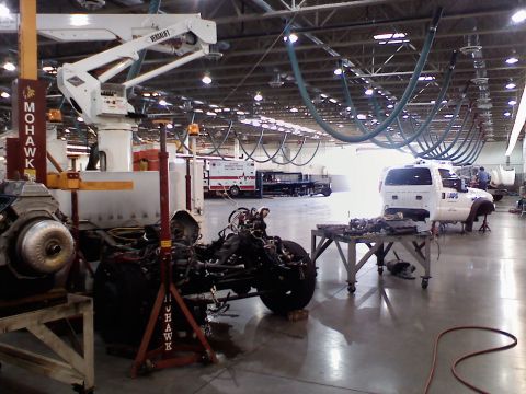 2001 Ford F-350 - A white pickup truck chassis sits in a workshop, with its engine and other parts disassembled and laid out on a table.