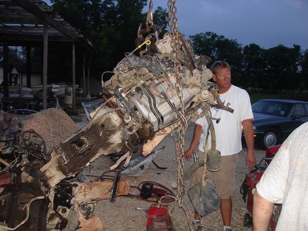 Engine and transmission assembly lifted by crane, with men nearby
