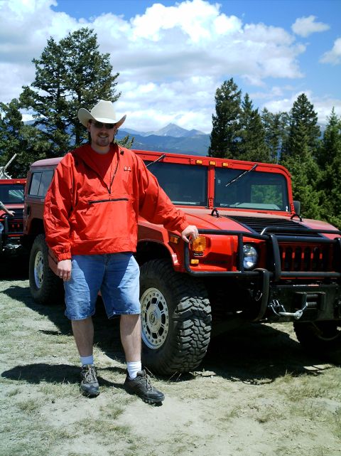 2000 Ford Crown Victoria - Man poses with a red Hummer H1 in a mountainous, wooded area under a cloudy sky.