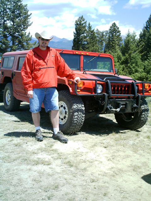 2000 Ford Crown Victoria - A man in a white cowboy hat and red windbreaker poses beside the front of a red Hummer H1 wagon fitted with a black brush guard, front winc…