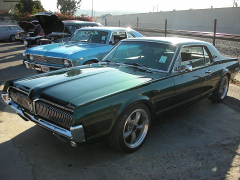 1998 Ford Crown Victoria - A green 1967 Mercury Cougar is parked next to other classic cars.