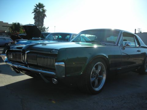 1998 Ford Crown Victoria - A green 1967 Mercury Cougar is parked at a car show, with other vehicles visible in the background.