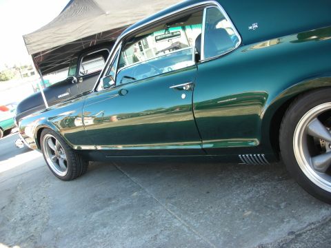 1998 Ford Crown Victoria - Dark green 1967 Mercury Cougar coupe with chrome trim and aftermarket wheels parked next to a black pickup truck.