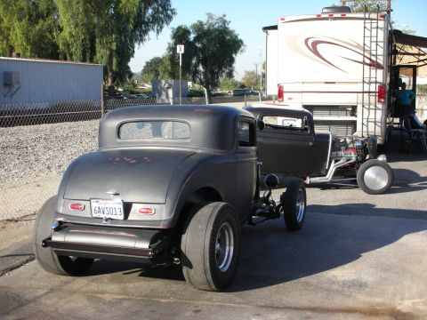 1998 Ford Crown Victoria - A custom hot rod coupe is parked next to a large RV on a sunny day.