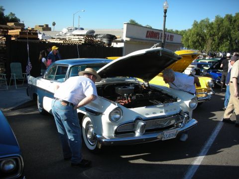 1998 Ford Crown Victoria - Two men inspect the engine bay of a vintage Plymouth Belvedere at an outdoor car show.