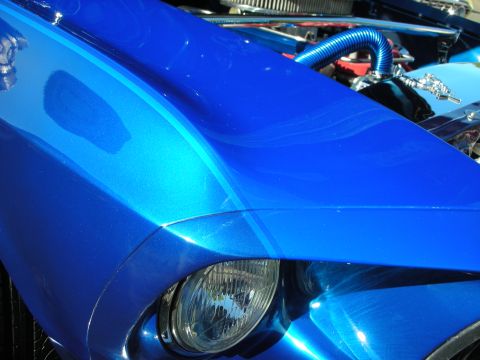 1998 Ford Crown Victoria - The metallic blue paint on this car has racing stripes and reflects the sunlight, revealing engine parts under the hood.