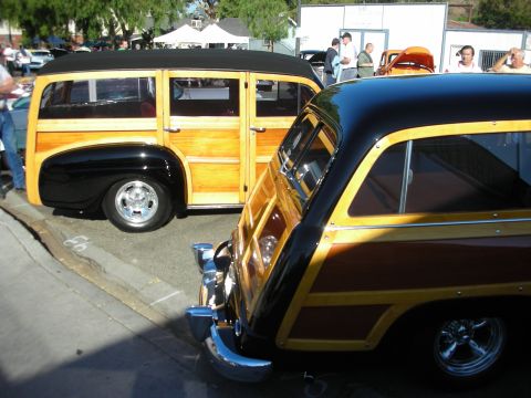 1998 Ford Crown Victoria - Two classic woodie station wagons are parked side-by-side, with the front vehicle partially obscuring the one behind it.