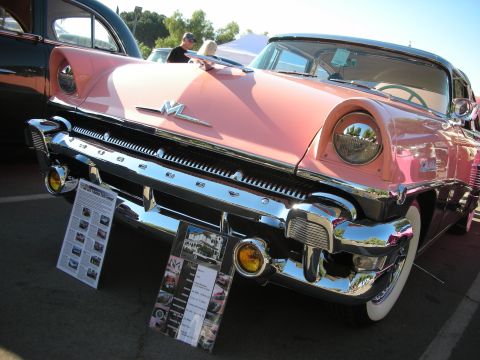 1998 Ford Crown Victoria - A vintage pink and black Mercury with extensive chrome details is displayed at an outdoor event.