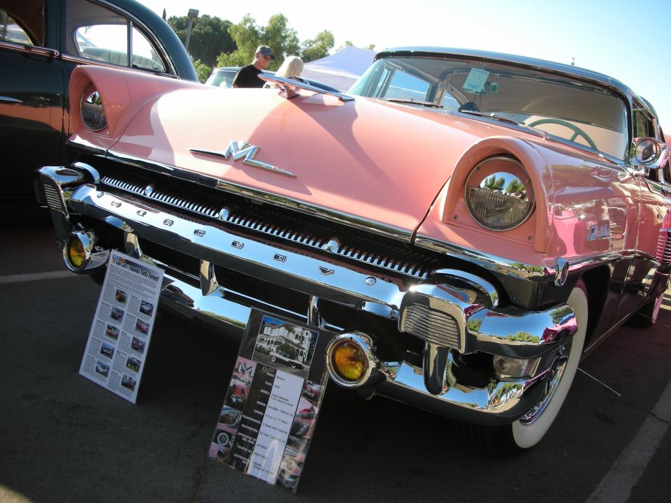 Pink and black Mercury with chrome grille and headlights, parked outdoors with informational signs