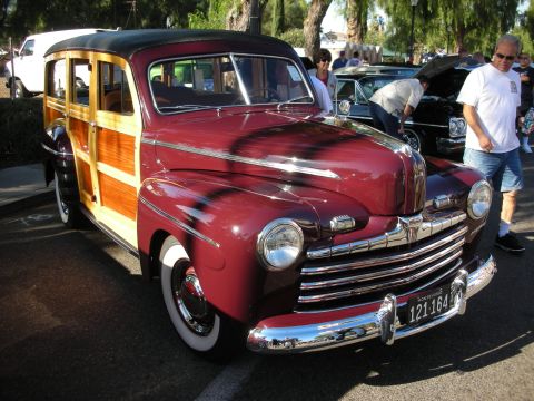 1998 Ford Crown Victoria - A classic woodie station wagon is parked at an outdoor event, with other vehicles and people in the background.