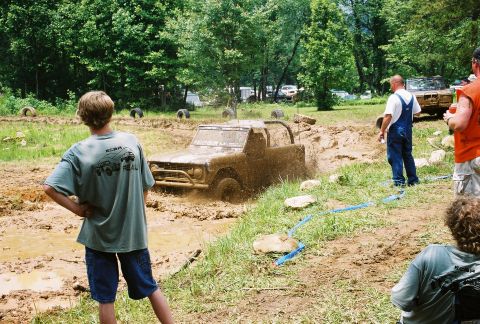1972 Ford Bronco - A 1972 Ford Bronco is driven through a muddy obstacle course with spectators watching.