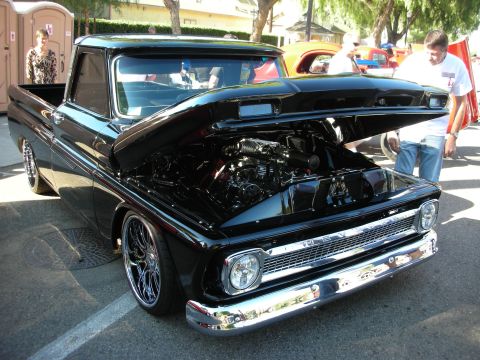 1998 Ford Crown Victoria - A black pickup truck from the 1960s is displayed with its hood open, a detailed engine and chrome accents.