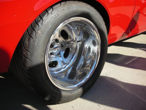 1998 Ford Crown Victoria - A close-up shot focuses on a shiny chrome wheel and tire on a red vehicle.