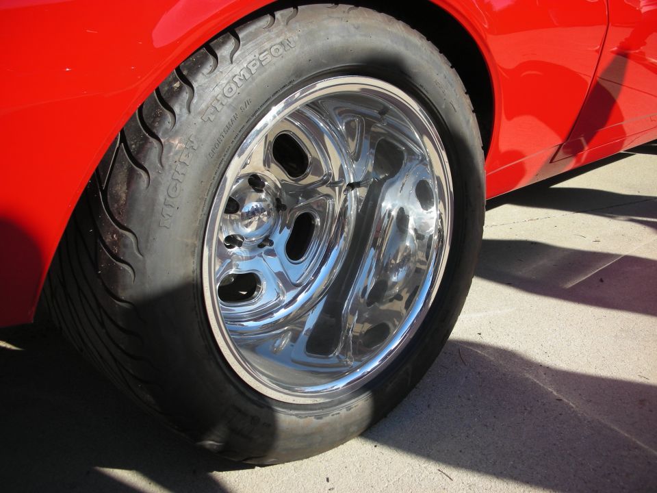 Close-up of a shiny chrome wheel on a red car. Tire has 'Mickey Thompson' text