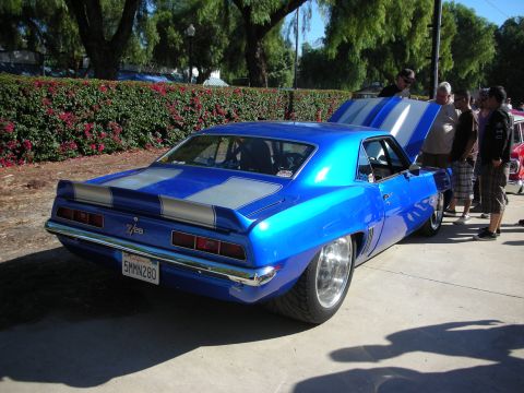 1998 Ford Crown Victoria - A bright blue 1969 Camaro with racing stripes is displayed with its hood open, drawing attention from onlookers.