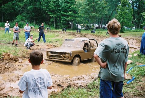 1972 Ford Bronco - A tan Ford Bronco is stuck in a mud pit while onlookers observe the scene.