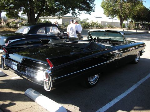 1998 Ford Crown Victoria - A black convertible is parked next to another black car, with two people standing between them.