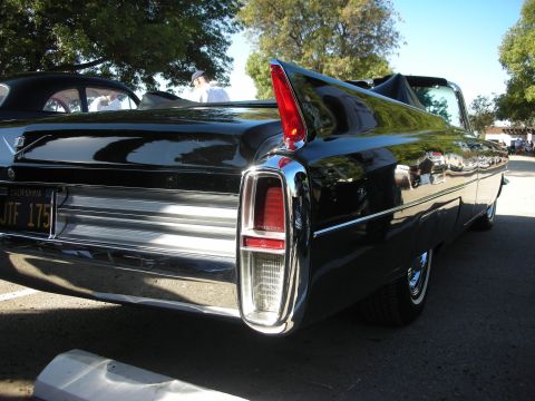 1998 Ford Crown Victoria - Rear view of a classic black convertible, possibly a 1960s Cadillac, with distinctive tail fins.