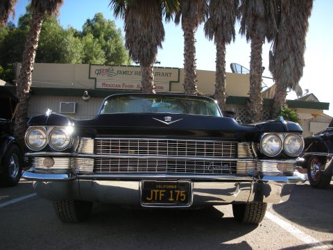1998 Ford Crown Victoria - A classic black Cadillac sits parked under palm trees in front of a family restaurant.