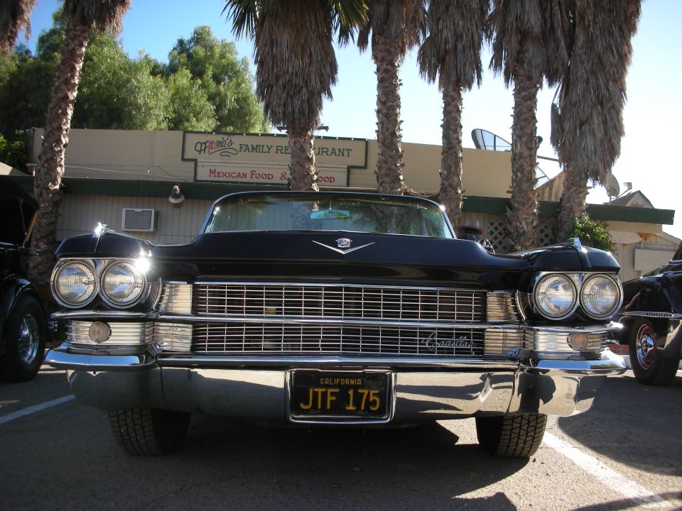 Front view of a black 1959 Cadillac Coupe de Ville parked in front of a restaurant