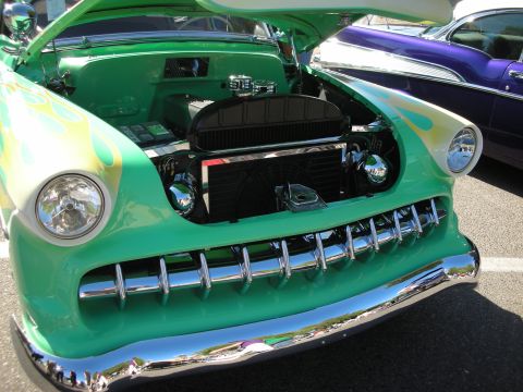 1998 Ford Crown Victoria - A green custom car with flames and an open hood is parked next to a purple car.