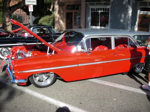 1998 Ford Crown Victoria - A classic red and silver sedan with custom wheels is parked on the street, with another car behind it.