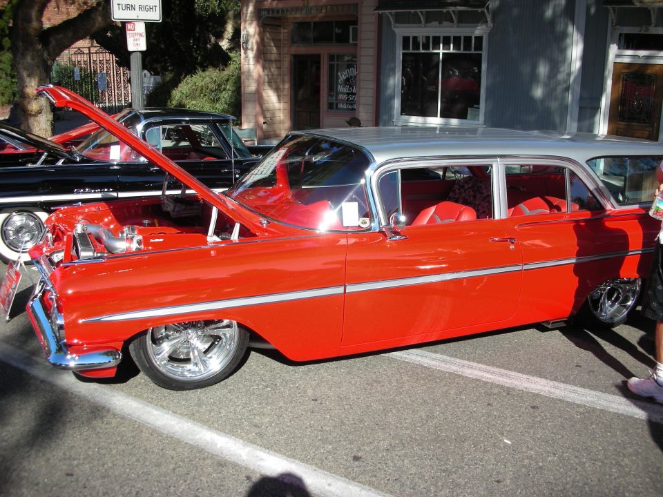 Red and silver two-door sedan with chrome wheels, lowered suspension, and red interior. Hood is open