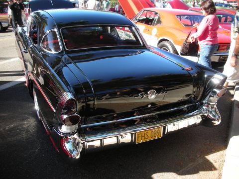 1998 Ford Crown Victoria - Rear view of a shiny black 1950s coupe, possibly a Buick Special, with prominent chrome details and a yellow license plate.