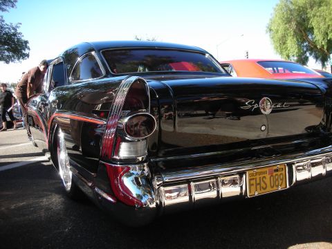 1998 Ford Crown Victoria - Rear view of a black 1955 Buick Special with chrome bumper and tail fins. Another car is visible behind.