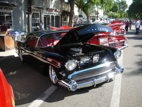 1998 Ford Crown Victoria - A black 1957 Buick is displayed with its hood open, its red interior and prominent chrome grille at an outdoor car show.